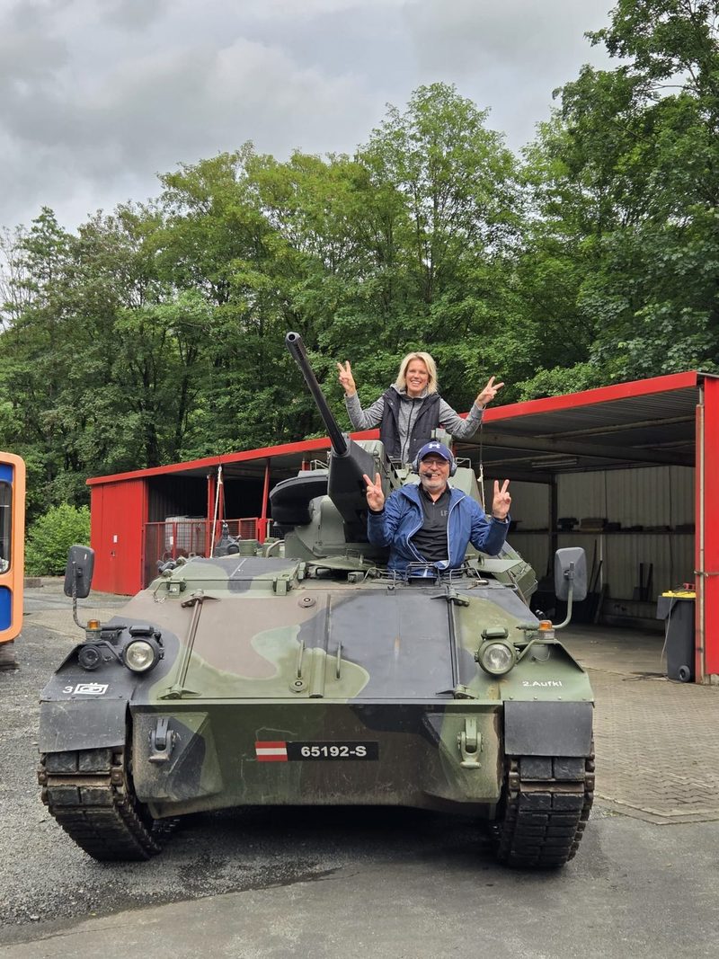 Gruppe von Gästen auf einem Kettenpanzer, die Arme in die Luft gestreckt
